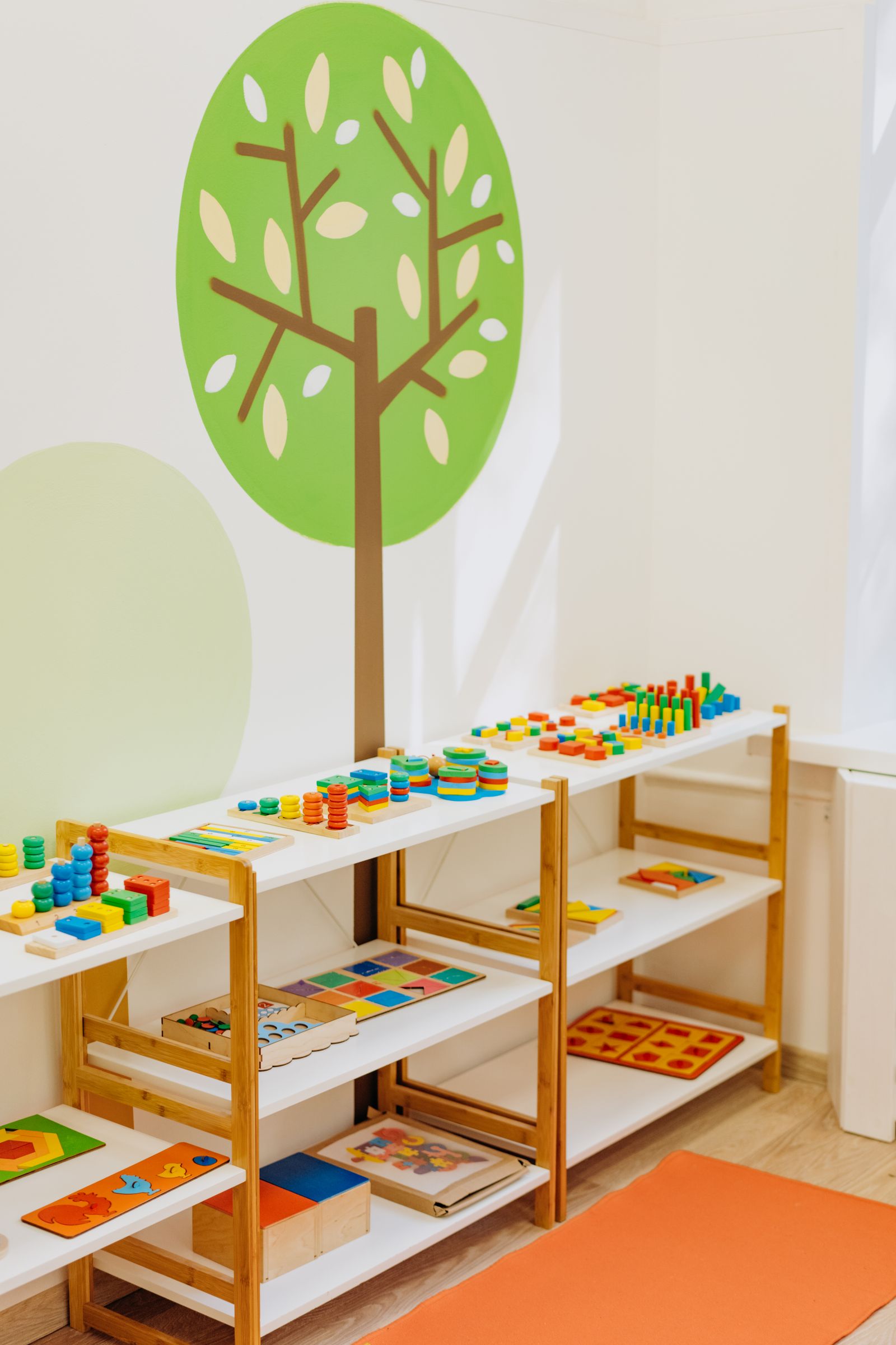 Low open shelves in a bright classroom, set at a child's height with wooden puzzles, stacking toys and sorting materials.