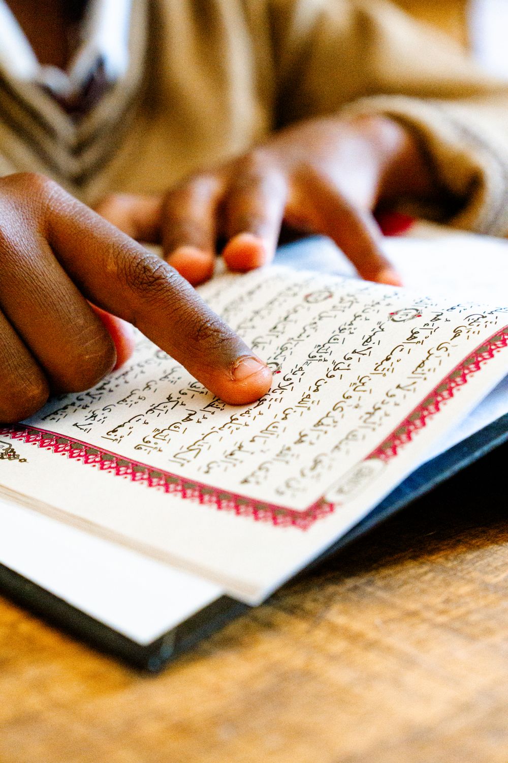 Close-up of a child's finger tracing a line of Arabic text in an open Qur'an.